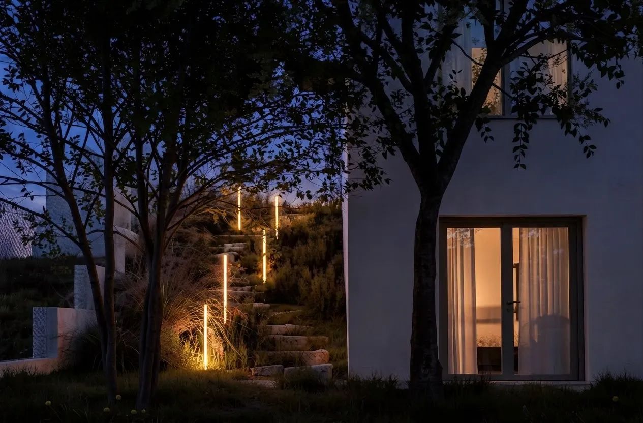 Casa MV — ușa-fereastră a parterului iluminată noaptea și scara exterioară pe pantă, marcată de stâlpi luminoși