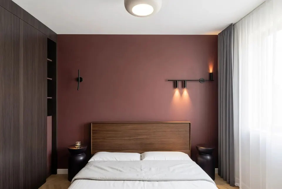 Apartament AD 1 — dormitor cu perete grena, tăblie din lemn riflat și aplice negre, lângă dulapul până în tavan